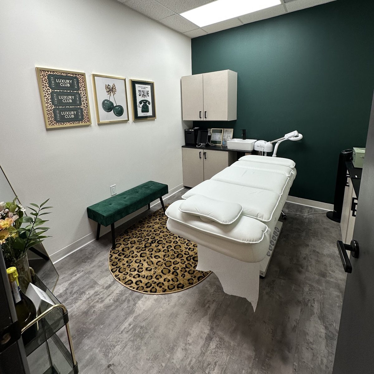 The treatment room at Bare Esthetics: a deep green accent wall, white waxing bed and leopard-print rug in the West Knoxville studio